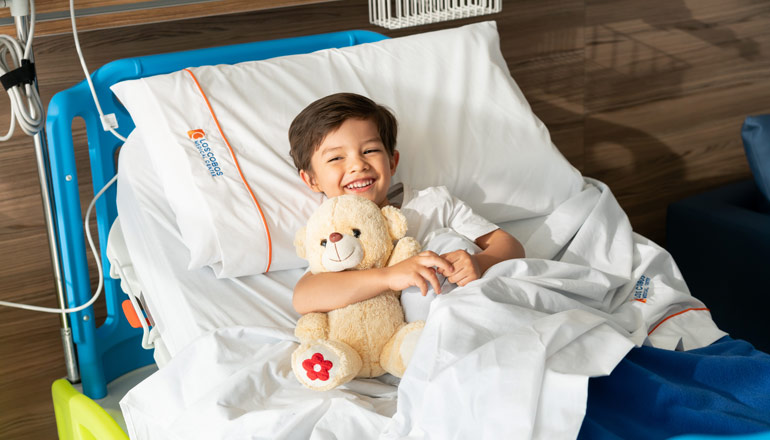 Boy holding teddy bear in hospital bed