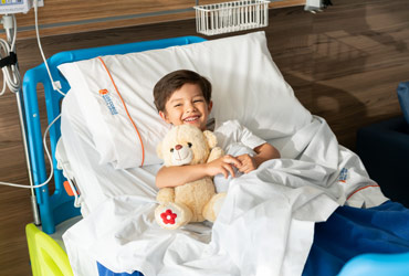 Boy holding teddy bear in hospital bed